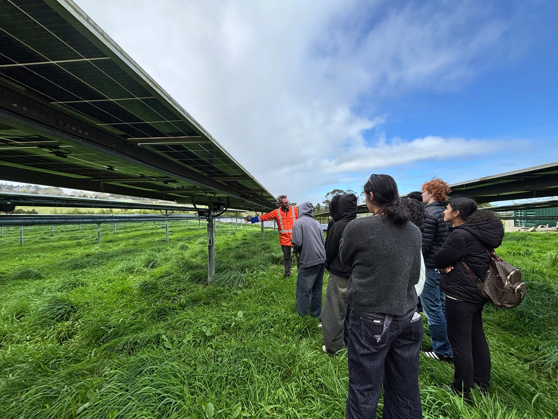 A group listening to a person speaking between solar panel rows
