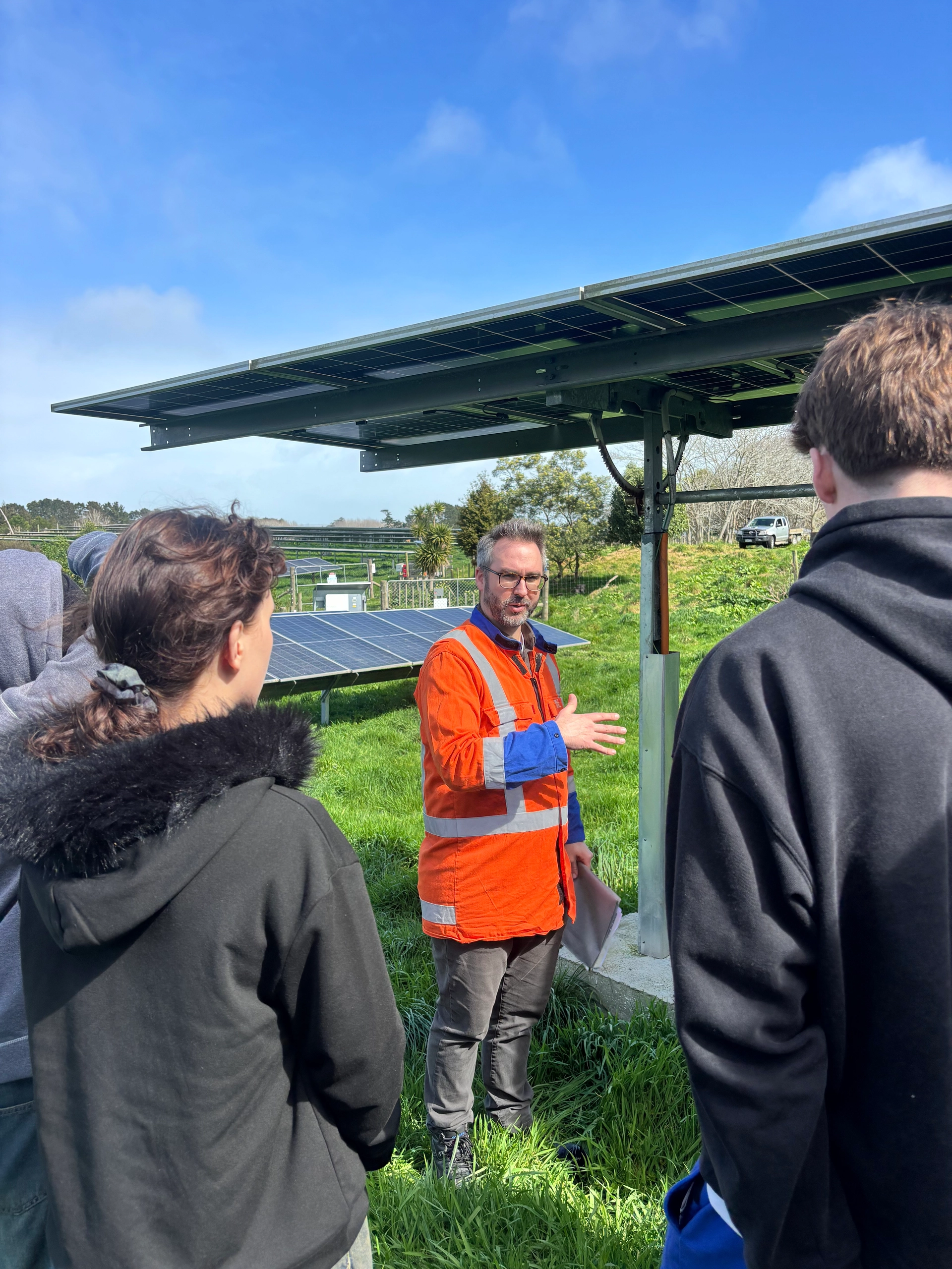 A person in orange high-visibility clothing speaking beneath a solar panel