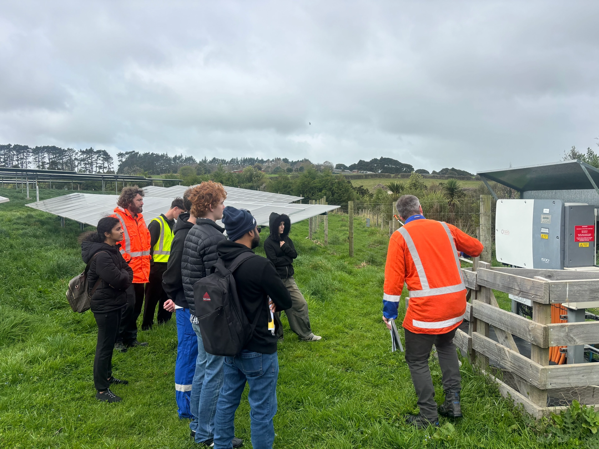 A group beside solar panels and an electrical equipment enclosure